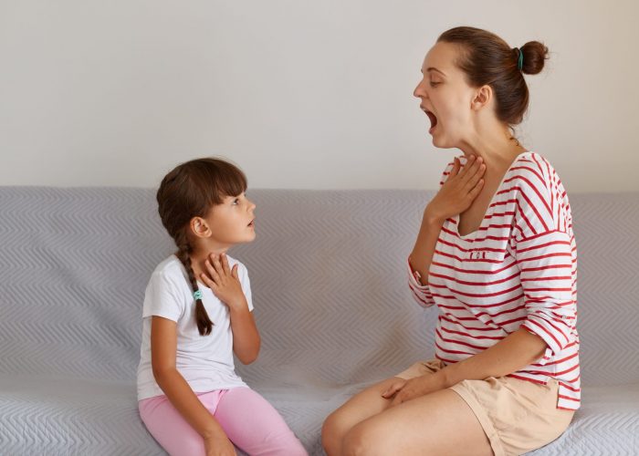 Side view portrait of speech pathologist demonstrating for little kid how to pronounce sounds right, Professional physiotherapist working on speech defects with small child girl indoors.